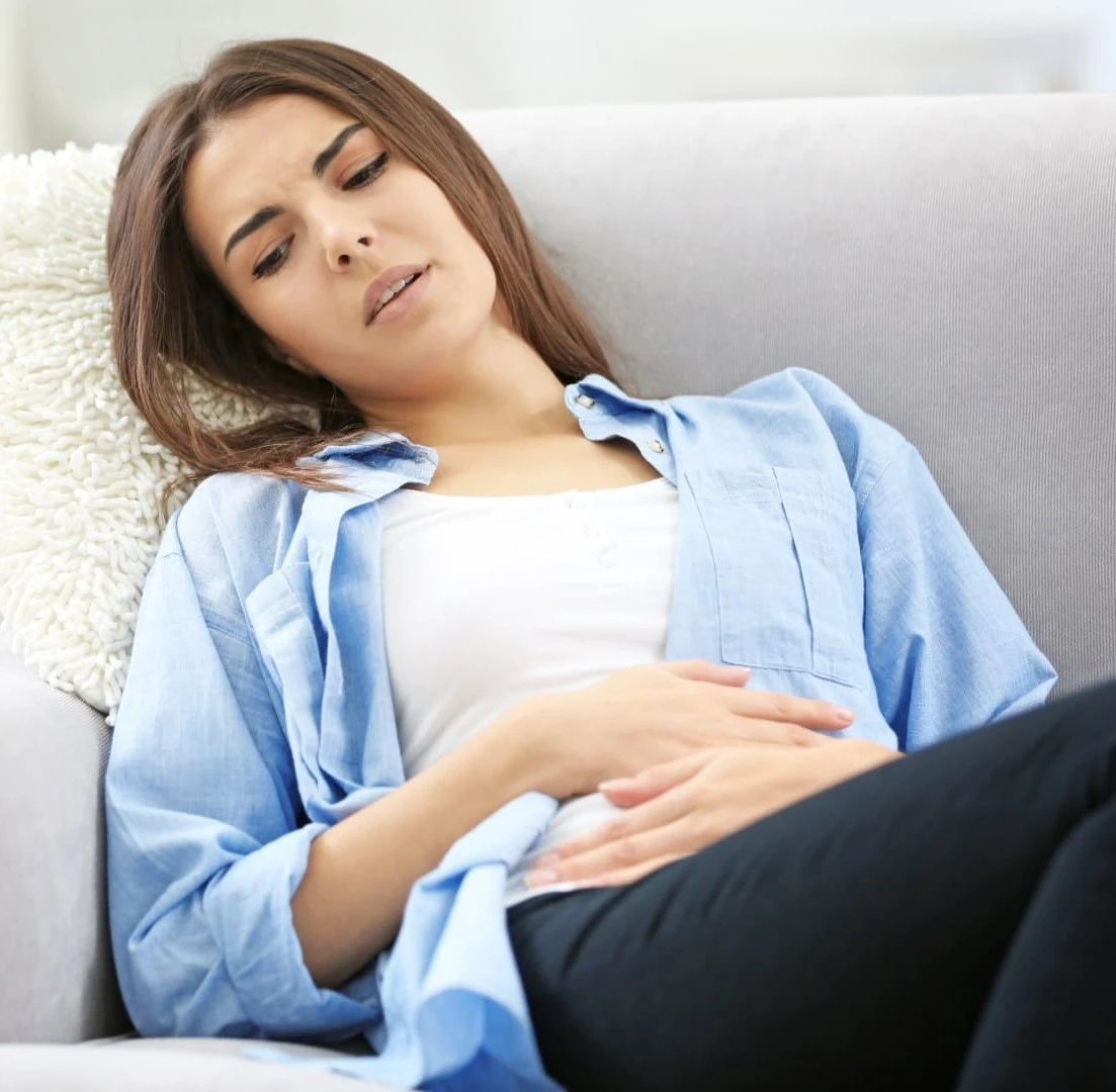 una donna accasciata sul divano con le mani sulla pancia dolente a causa dei problemi gastrici