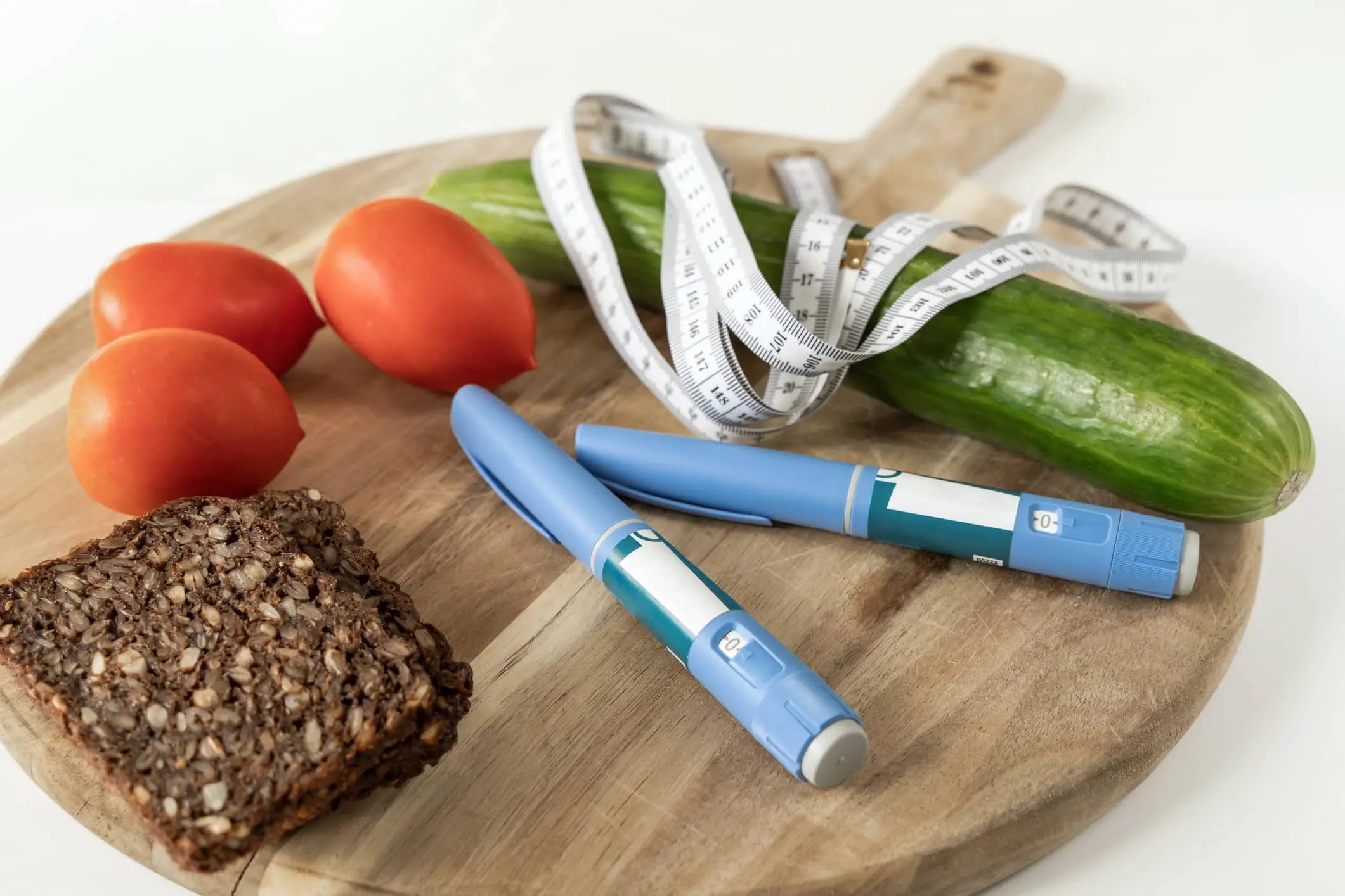 un tagliere che presenta dei pomodorini, una zucchina e una fetta di pane ai cereali con accanto due pennette contenenti i principi attivi dei farmaci dimagranti