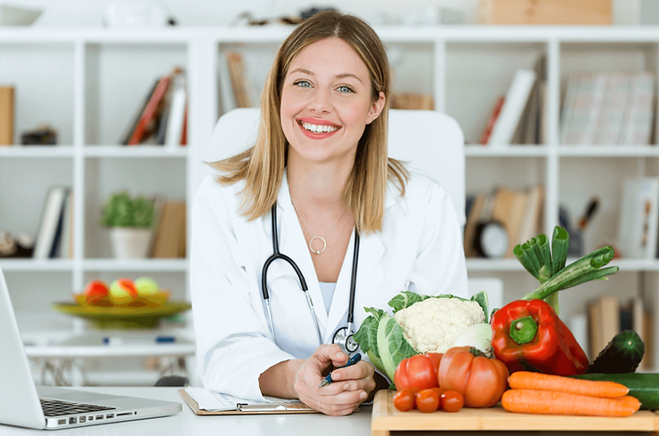 una nutrizionista con camice bianco seduta dietro una scrivania con sopra delle verdure salutari