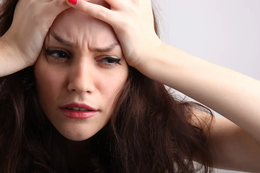 Donna con espressione di disagio che tiene le mani sulla fronte, illustrando possibili effetti collaterali come mal di testa o malessere associati alla semaglutide.