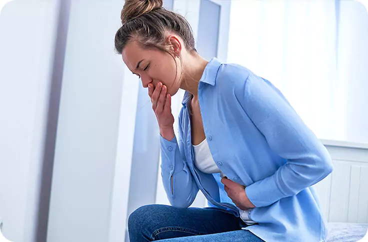 Donna in camicia azzurra che mostra segni di nausea e disagio addominale, due dei più comuni effetti collaterali gastrointestinali associati al trattamento con tirzepatide.